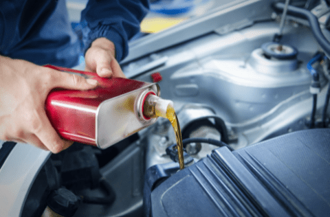 Technician pouring engine oil into car engine during maintenance at Hillside Auto Clinic.