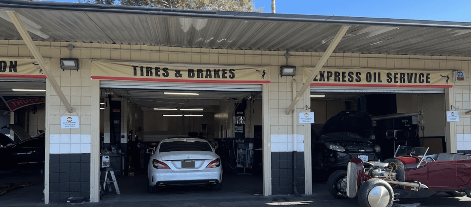 Auto repair shop with cars and vintage vehicle in front.