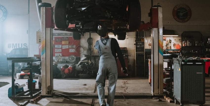 Auto repair technician inspecting vehicle on hydraulic lift.