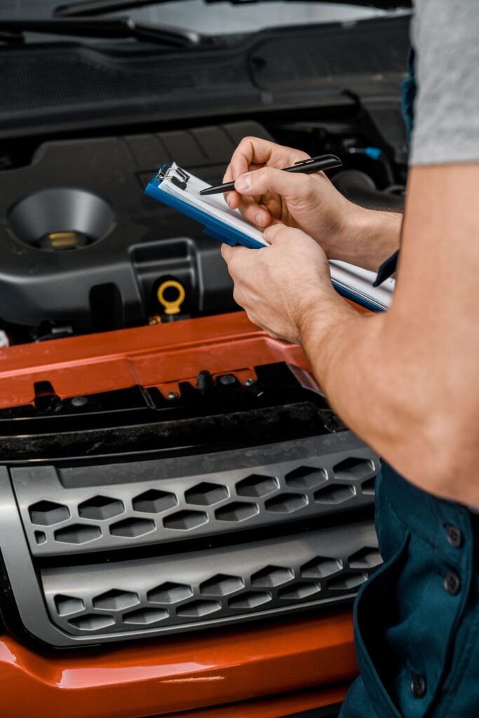 Auto mechanic inspecting car engine with clipboard and pen.