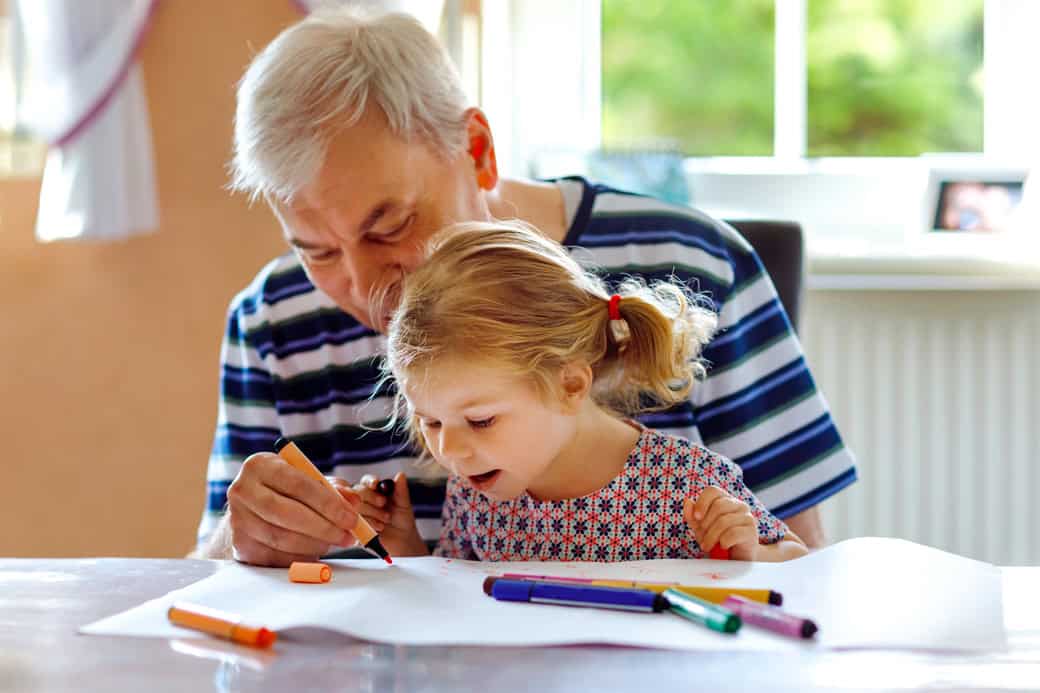 Cute little baby toddler girl and handsome senior grandfather painting with colorful pencils at home. Grandchild and man having fun together