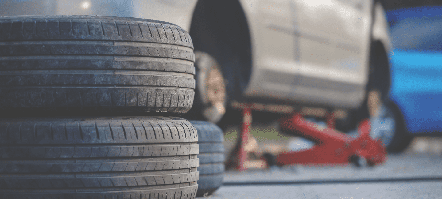 Close-up of stacked tires with a car on a hydraulic lift in the background.