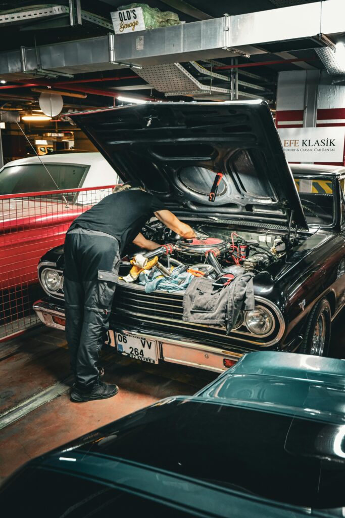 Automotive mechanic inspecting engine under the hood of a classic car at Honest Engine of Roseville.