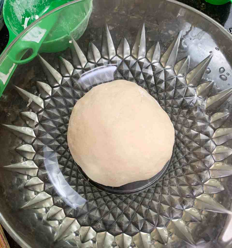 Freshly kneaded dough resting in a decorative glass bowl for traditional Pacific Island bread recipes.