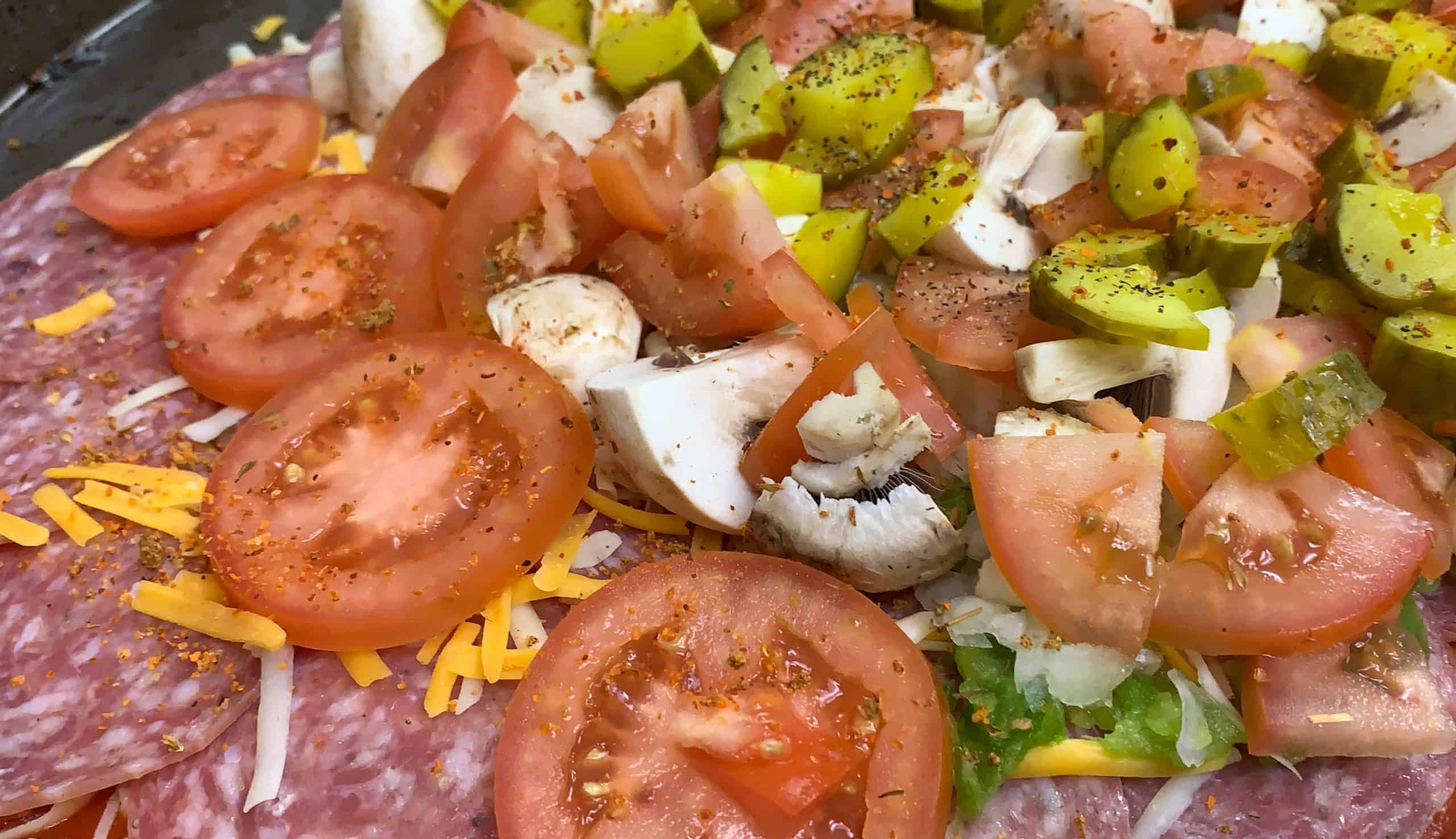 Fresh vegetable pizza with sliced tomatoes, pickles, mushrooms, and shredded cheese.