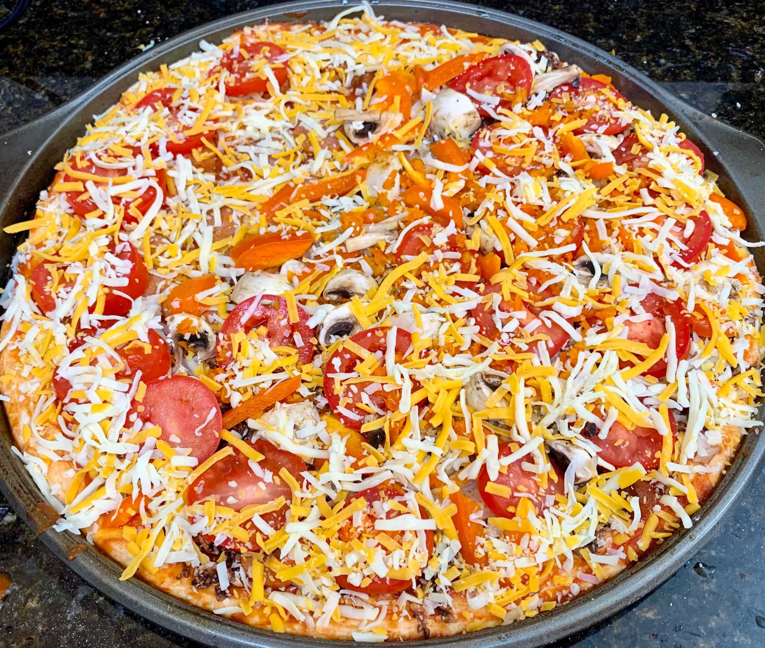 Freshly prepared Hawaiian pizza with cheese, tomatoes, peppers, and mushrooms on a black countertop.
