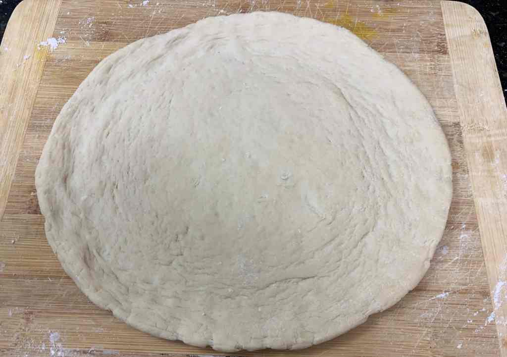 Soft dough ready for baking or cooking on a wooden surface with flour sprinkled around.
