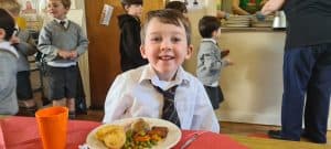 Young boy enjoying school lunch at Inchmarlo in a lively classroom.
