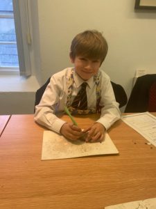 Young boy writing at desk in classroom, school environment, engaged in learning activity.