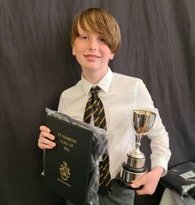 Young boy in school uniform holding a trophy and certificate.