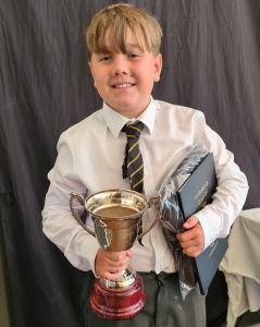 Young boy smiling with trophy and books at Inchmarlo School.