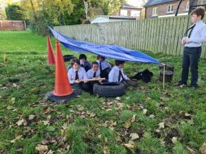 Students exploring outdoor classroom at Inchmarlo school with makeshift shelter.