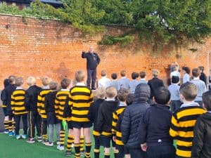 Students in school uniforms listening to a speaker outdoors.