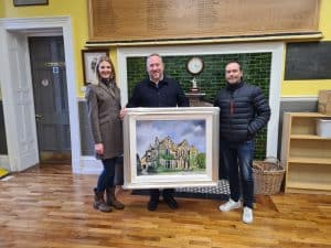 Three people holding a framed painting in a cozy indoor setting, showcasing art and hospitality at Inchmarlo.
