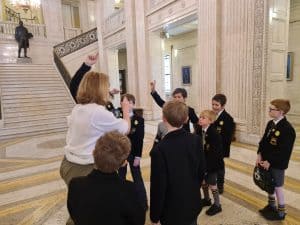 Group of children and teacher engaging in a discussion inside a grand building.
