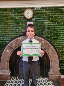Young boy holding a diploma in front of a fireplace at Inchmarlo School, celebrating achievement.