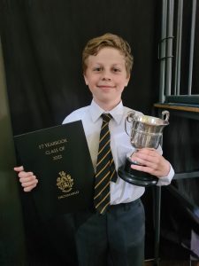 Young student holding trophy and certificate at Inchmarlo School, showcasing academic and extracurricular success.