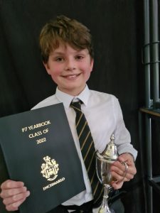 Young student holding a yearbook and trophy, proudly celebrating academic achievement.