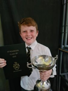 Happy student with trophy and award certificate in school uniform.