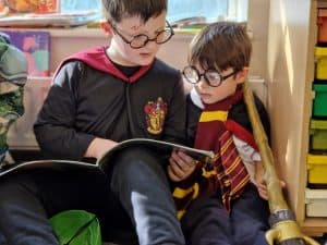 Two children wearing Harry Potter costumes reading a book together.
