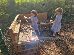 Two children playing in an outdoor enclosed play area with sand and soil.