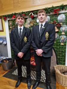 Two young boys in formal school uniforms at Inchmarlo, standing indoors with festive decorations.
