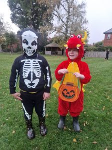 Two children dressed in Halloween costumes outdoors, one as a skeleton and the other as a dragon, celebrating festive occasion.