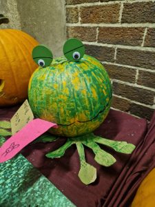 Colorful pumpkin craft with googly eyes and paper legs, displayed on a table.