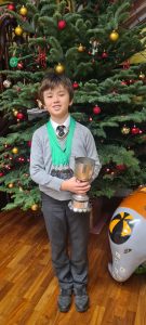 Young boy holding a trophy in front of a Christmas tree.
