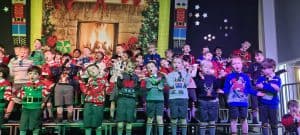 Children singing Christmas carols on stage at Inchmarlo holiday event.