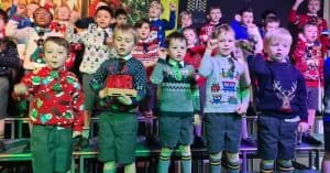 Children singing at Inchmarlo Christmas event in festive sweaters.