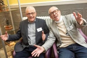 Two smiling men in suits at Inchmarlo, enjoying a social moment.