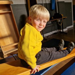 Smiling young boy in yellow sweatshirt sitting on wooden bench at Inchmarlo.