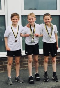 Three young boys smiling with medals and trophy, outdoor sports event, Inchmarlo.