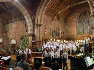 Large choir performing in historic church setting with Christmas tree and flags in the background.