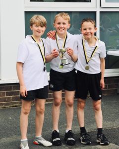 Three children wearing medals and sports uniforms outside Inchmarlo school.