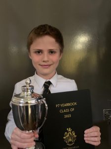 Young student holding a trophy and school book, celebrating academic achievement at Inchmarlo.