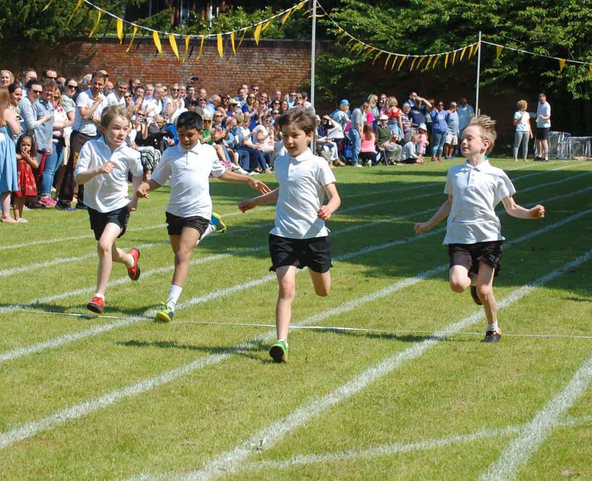 Children race on outdoor athletics track with cheering crowd and colorful decorations.