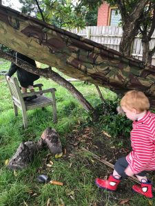 Young boy enjoying nature near fallen tree and dog in a lush garden setting.