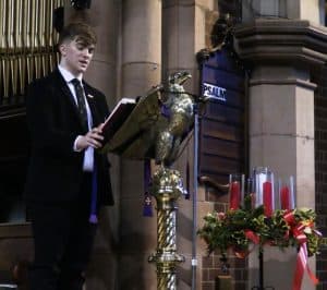 Aspiring student reading during remembrance event at Inchmarlo with floral tribute and candles.