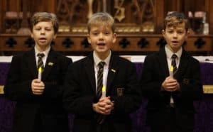 Three boys in uniform holding candles at Inchmarlo School event.