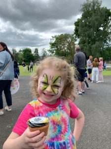 Smiling girl with face paint holding cupcake at Inchmarlo outdoor event.