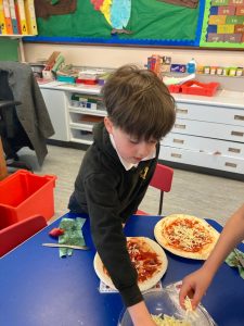 Child preparing pizza in classroom kitchen.