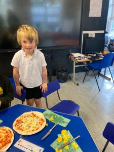 Young student standing in classroom with pizza on table.