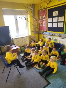Young children in yellow uniforms sitting and listening during classroom activity.