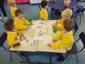 Young children in yellow smocks engaging in creative arts at Inchmarlo preschool.