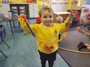 Young boy holding colorful toy chain in classroom.