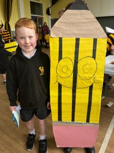 Young boy in school uniform standing beside colorful art project in school hall.