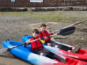 Two children enjoy kayaking at Inchmarlo amid a scenic outdoor setting.