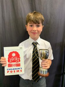 Young boy in school uniform holding a trophy and poetry book at Inchmarlo.